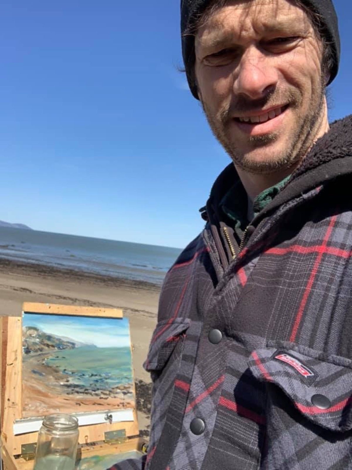 Jean Delisle sur une plage du fjord, chevalet de plein air et petite toile en cours derrière lui