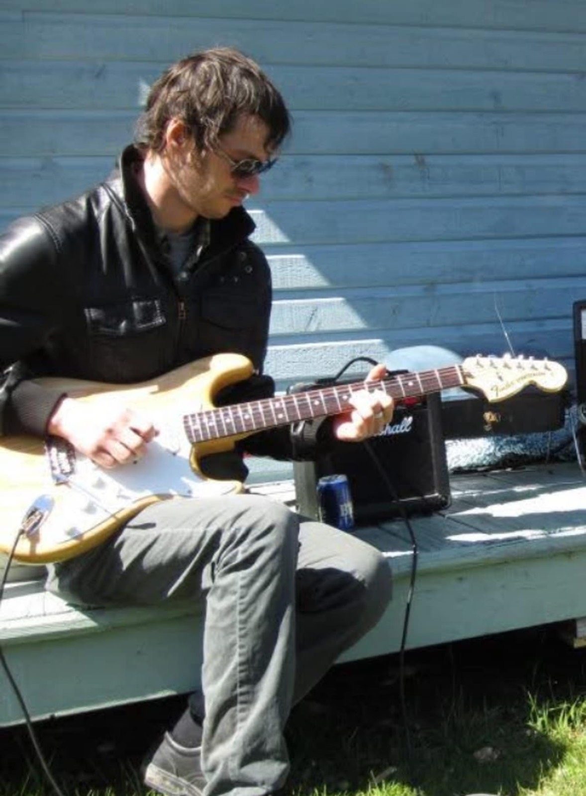 Jean Delisle joue d'une guitare électrique Stratocaster, assis devant un petit ampli