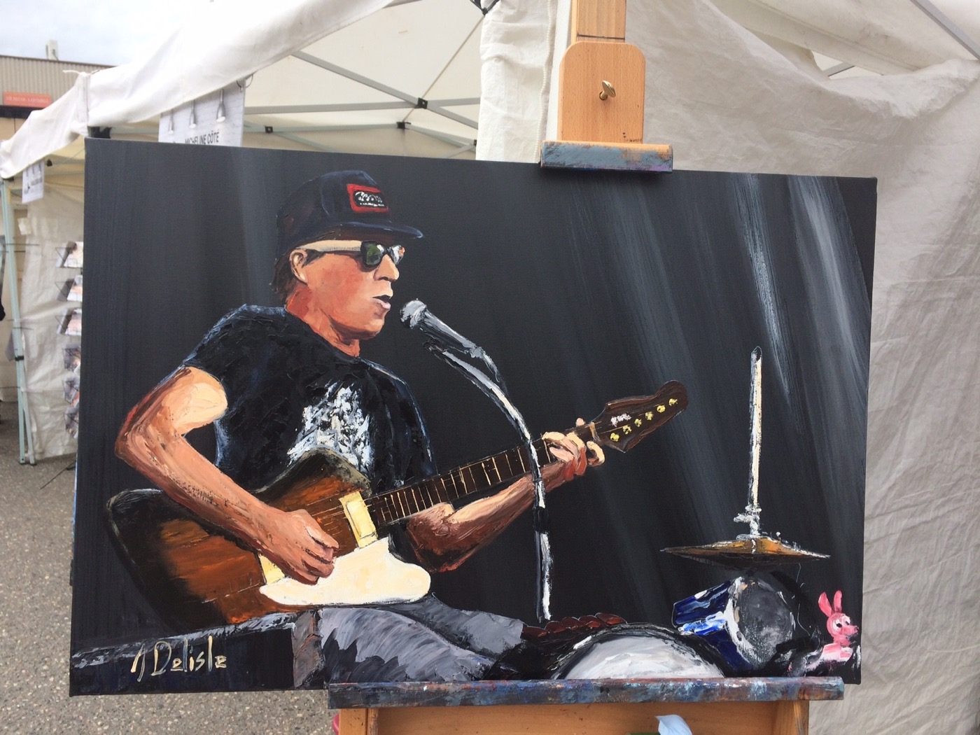Toile de Fred Fortin à la guitare, peinte à l'huile sur fond noir, posée sur un chevalet sous la tente du symposium à Alma
