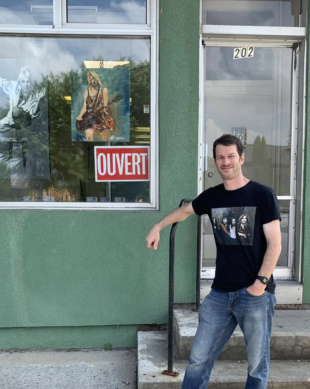 Jean Delisle devant la porte de sa galerie, affiche OUVERT dans la vitrine