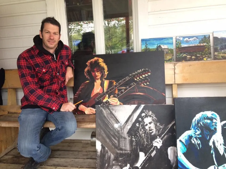 Jean Delisle assis à côté de ses toiles de musiciens à son kiosque du Happening de Tadoussac