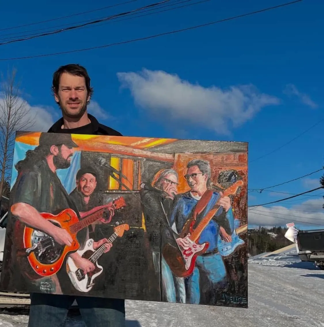Jean Delisle tient la toile Le blues c'est la vie dehors, sous un ciel bleu