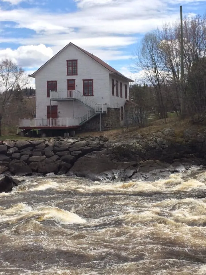 Le vrai Moulin Riverin, bâtiment blanc au toit rouge au-dessus des rapides