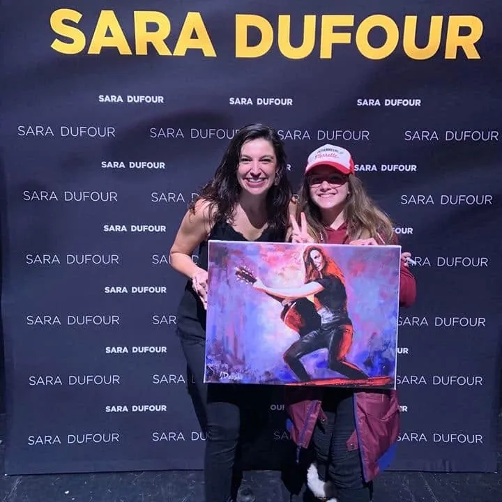 Deux personnes tiennent l'impression sur toile du portrait devant un mur Sara Dufour
