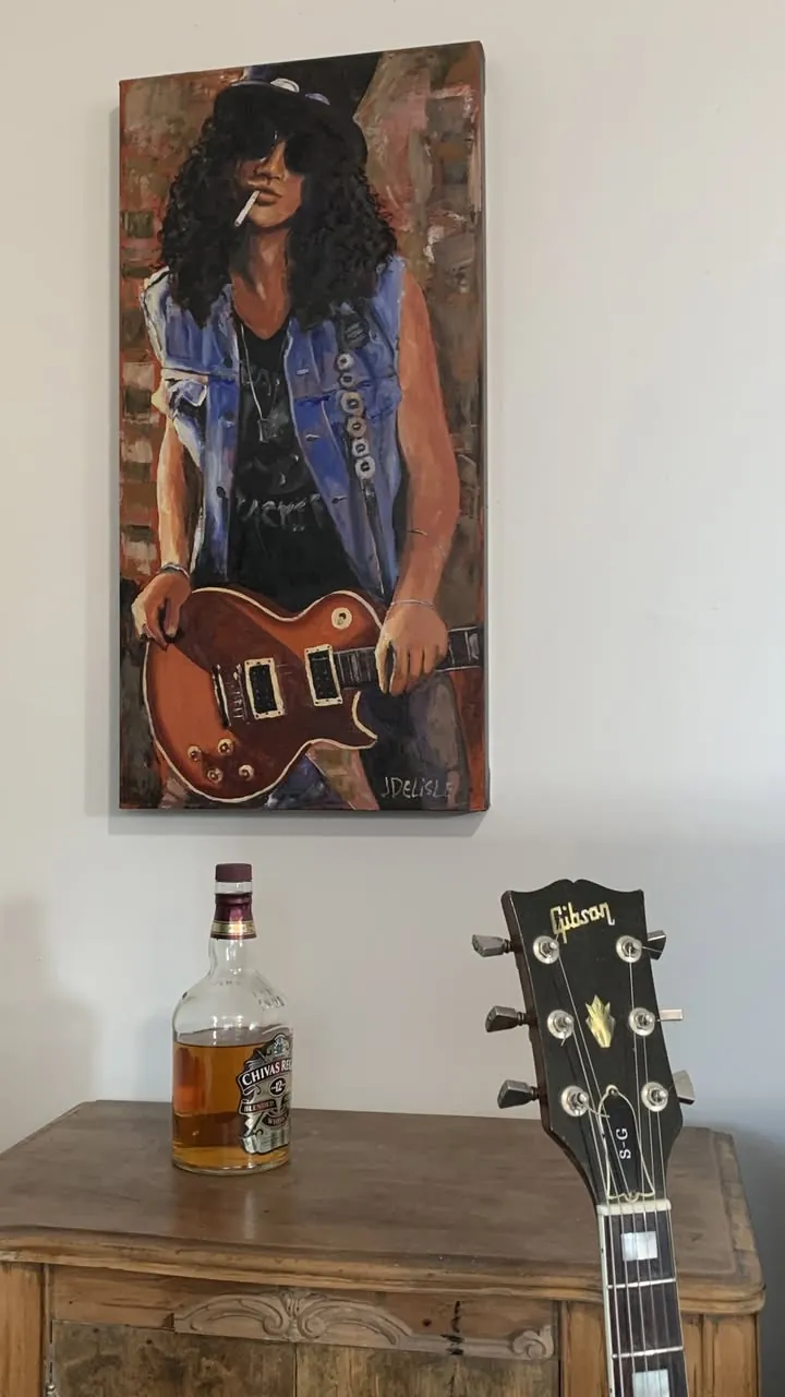 Slash et sa Les Paul accrochée au mur au-dessus d'une vraie guitare Gibson et d'une bouteille