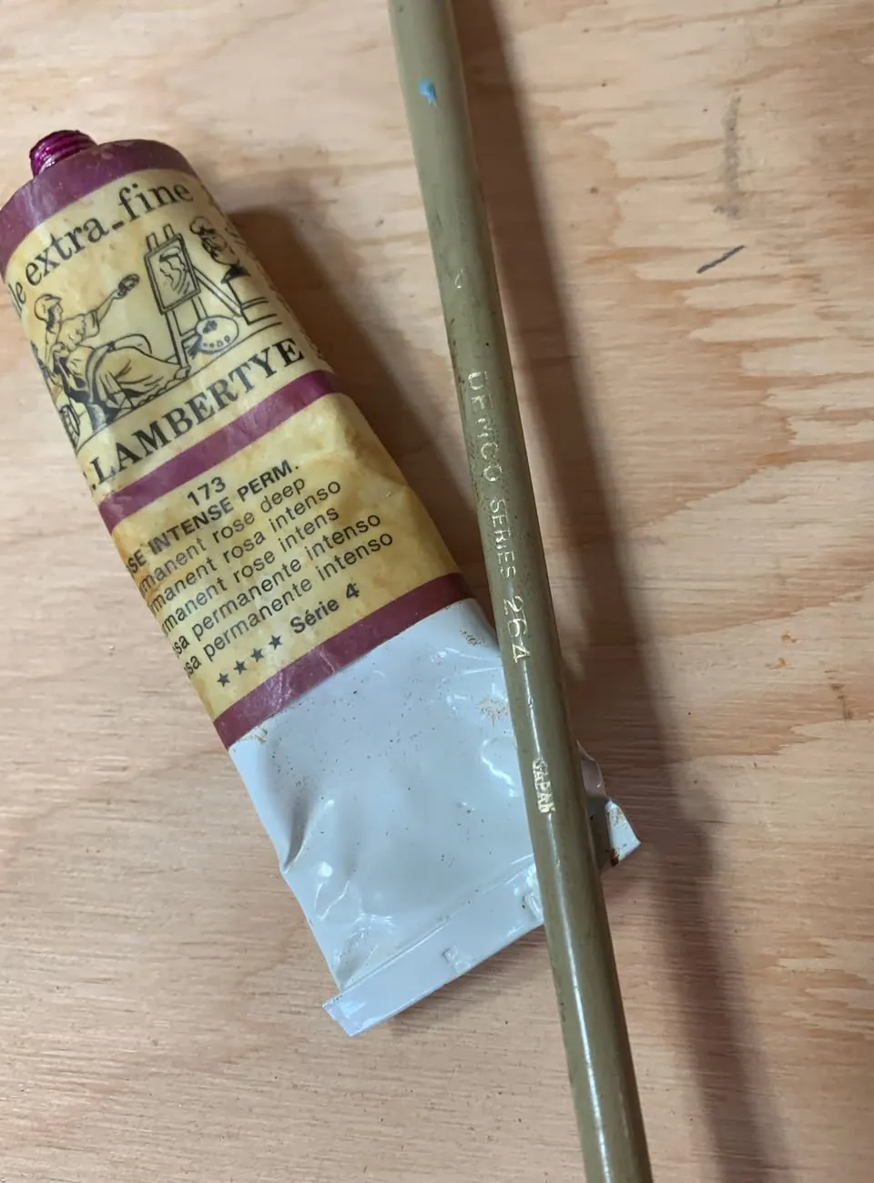 Vieux tube de peinture à l'huile Rosa permanente intenso posé sur une planche de bois, avec un pinceau